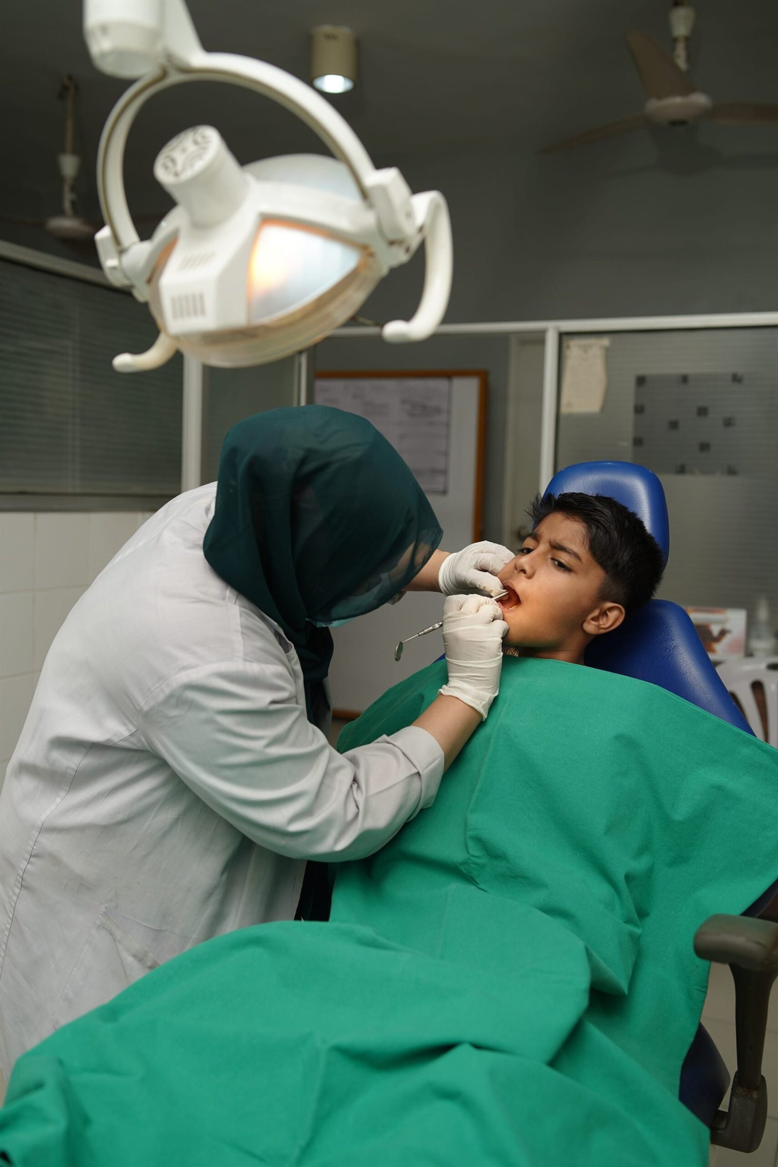 Dentist treating a young patient in the dental treatment chair at PEBS Hospital