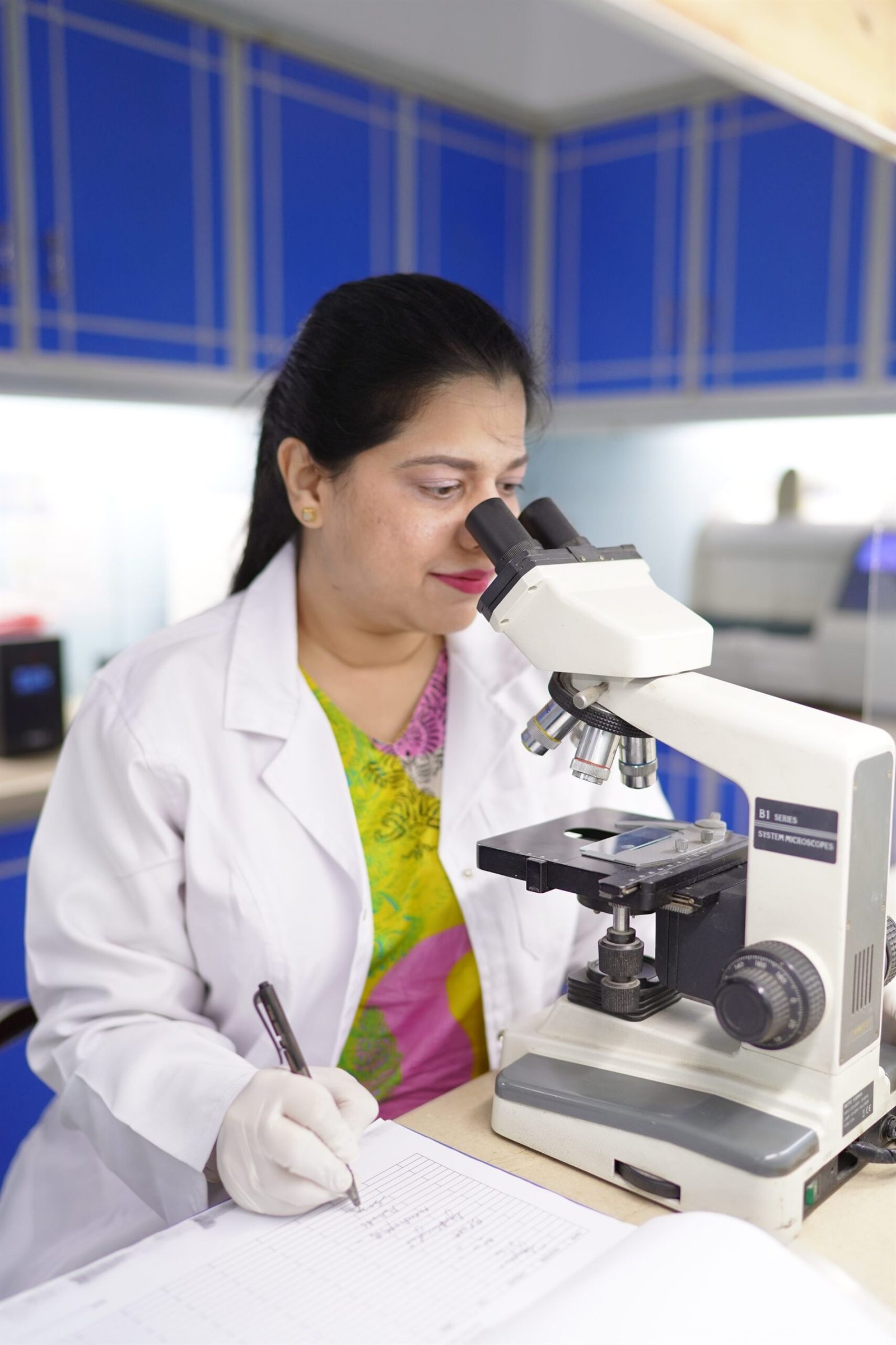 Laboratory technologist examining samples under a microscope at PEBS Hospital